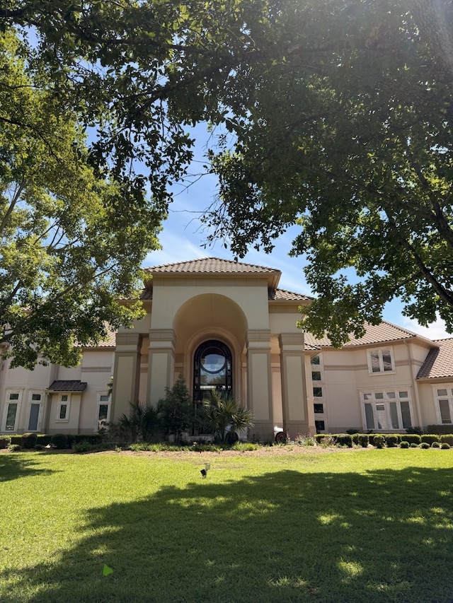mediterranean / spanish-style home with a tile roof, a front yard, and stucco siding