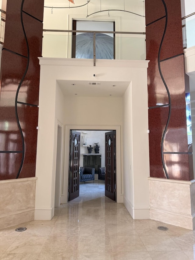 hallway with baseboards, visible vents, marble finish floor, and a towering ceiling
