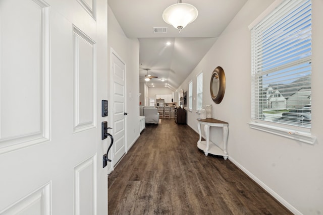 hallway featuring dark wood-type flooring, visible vents, baseboards, and lofted ceiling