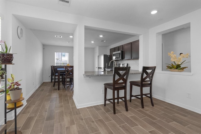 kitchen featuring stainless steel microwave, fridge, dark brown cabinets, and wood finished floors