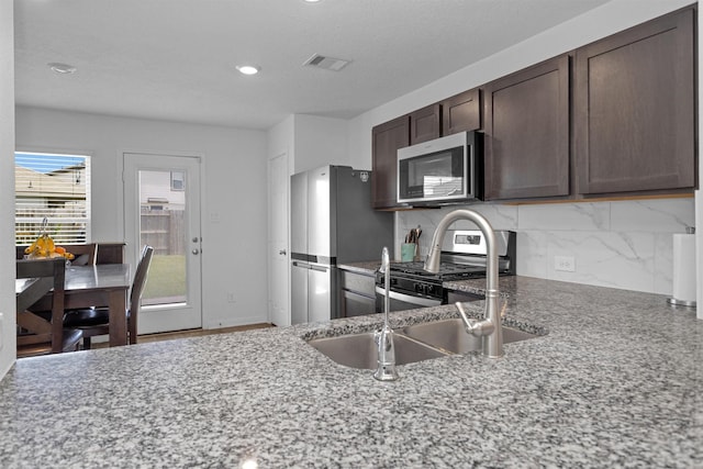 kitchen featuring dark brown cabinetry, tasteful backsplash, visible vents, a sink, and stainless steel appliances