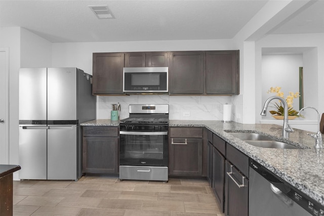 kitchen featuring dark brown cabinetry, light stone counters, visible vents, stainless steel appliances, and a sink