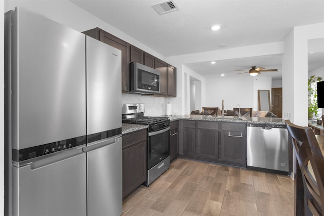 kitchen featuring visible vents, a sink, dark brown cabinets, stainless steel appliances, and stone countertops