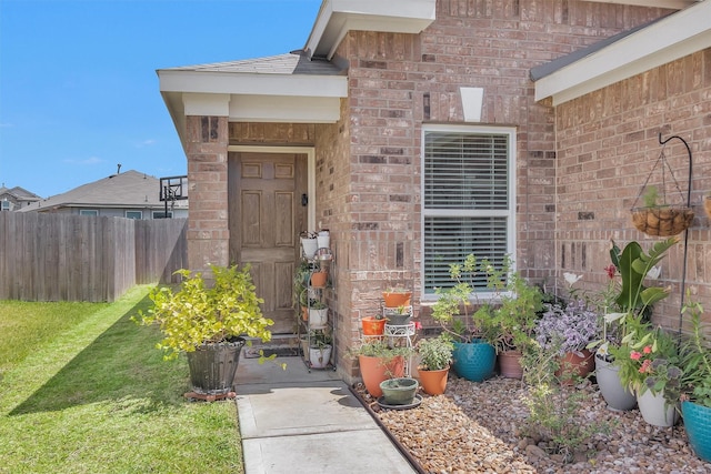 property entrance with brick siding, fence, and a lawn