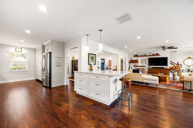 kitchen featuring freestanding refrigerator, a kitchen breakfast bar, white cabinets, visible vents, and open floor plan