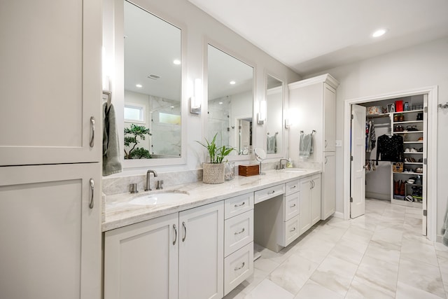 full bath featuring a stall shower, double vanity, a sink, and a walk in closet
