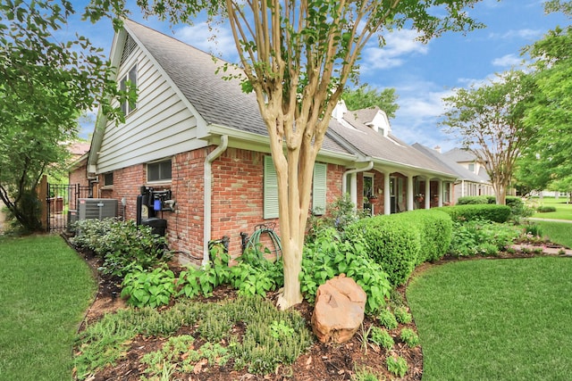view of home's exterior featuring roof with shingles, a yard, central AC unit, and brick siding