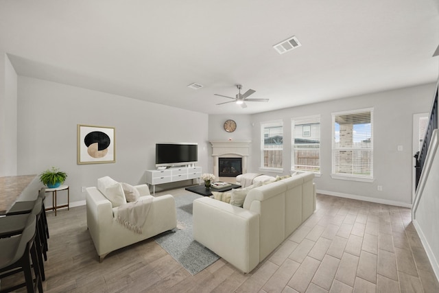 21406 Tropisea Dr, Cypress, TX 77433 - living area featuring light wood-style floors, a glass covered fireplace, a ceiling fan, visible vents, and baseboards