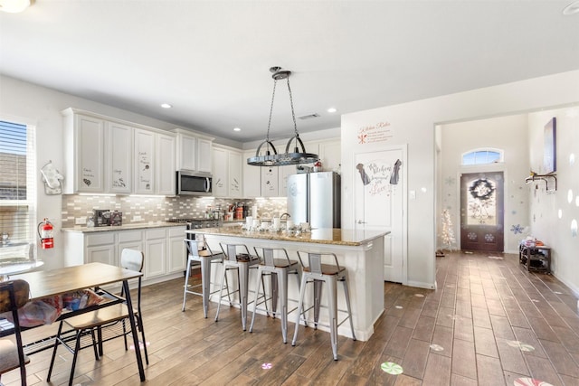 kitchen with freestanding refrigerator, an island with sink, stainless steel microwave, wood finished floors, and a breakfast bar area