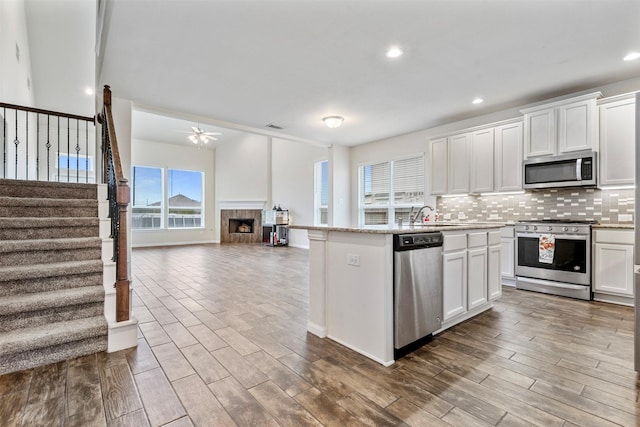 kitchen featuring open floor plan, a ceiling fan, a center island with sink, decorative backsplash, and appliances with stainless steel finishes