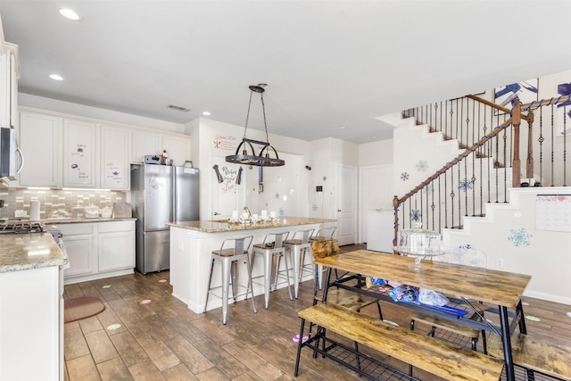 kitchen featuring a breakfast bar, a kitchen island, white cabinets, stainless steel appliances, and wood finished floors