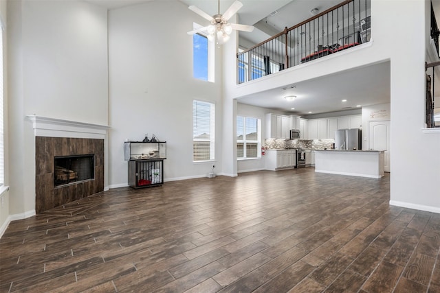 living room featuring a tile fireplace, dark wood-type flooring, a towering ceiling, and a ceiling fan