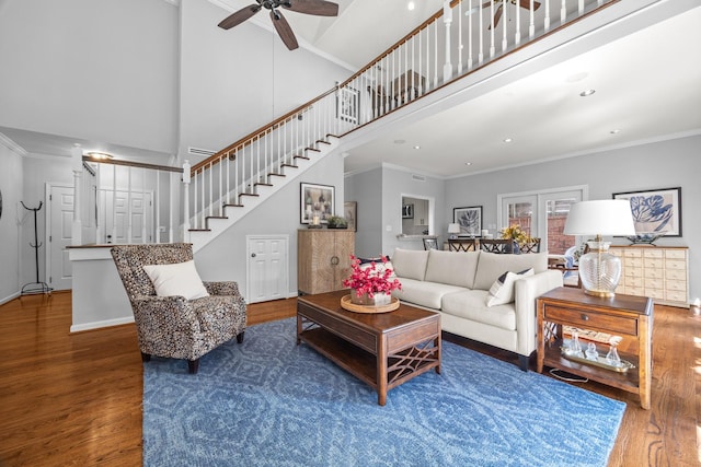 living room with wood finished floors, stairway, a ceiling fan, a high ceiling, and crown molding