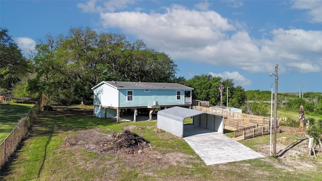 rear view of property with a carport, driveway, fence, and an outdoor structure