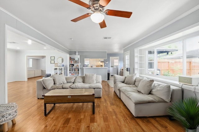 living room featuring crown molding, a ceiling fan, light wood finished floors, and visible vents