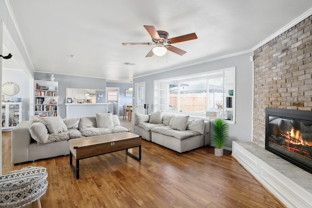 living room featuring visible vents, crown molding, wood finished floors, a fireplace, and a ceiling fan