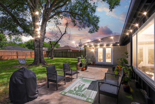 patio terrace at dusk with a lawn, french doors, and a fenced backyard