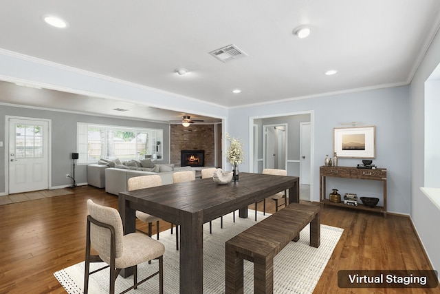 dining room with ornamental molding, a brick fireplace, wood finished floors, and visible vents