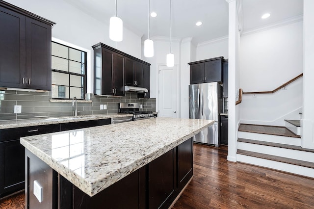 kitchen featuring a kitchen island, under cabinet range hood, a sink, stainless steel appliances, and decorative backsplash