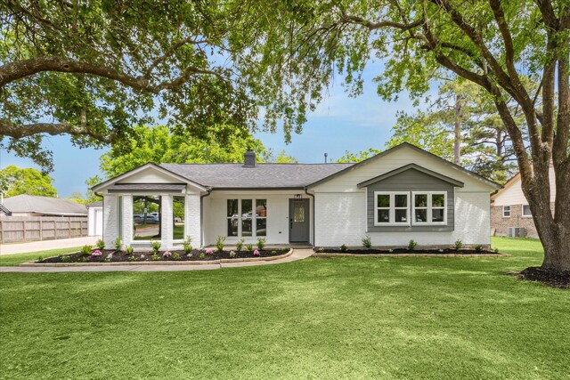 ranch-style house with a chimney, a front lawn, brick siding, fence, and a shingled roof