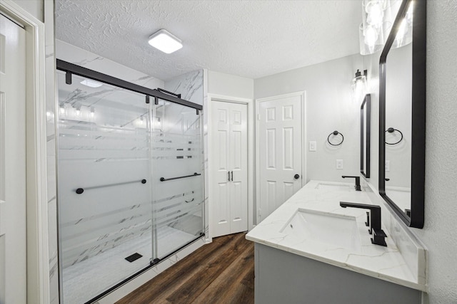 full bathroom with a textured ceiling, wood finished floors, a sink, a marble finish shower, and double vanity