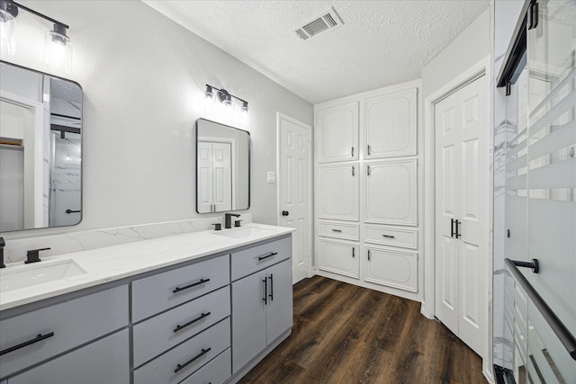 bathroom with a sink, visible vents, double vanity, and wood finished floors