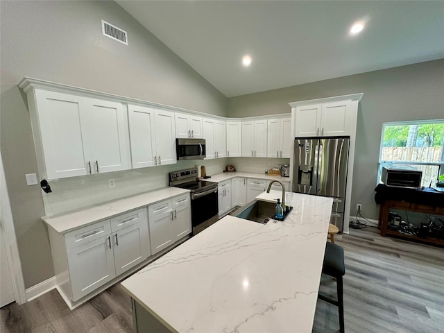 kitchen with visible vents, a sink, a kitchen bar, wood finished floors, and stainless steel appliances