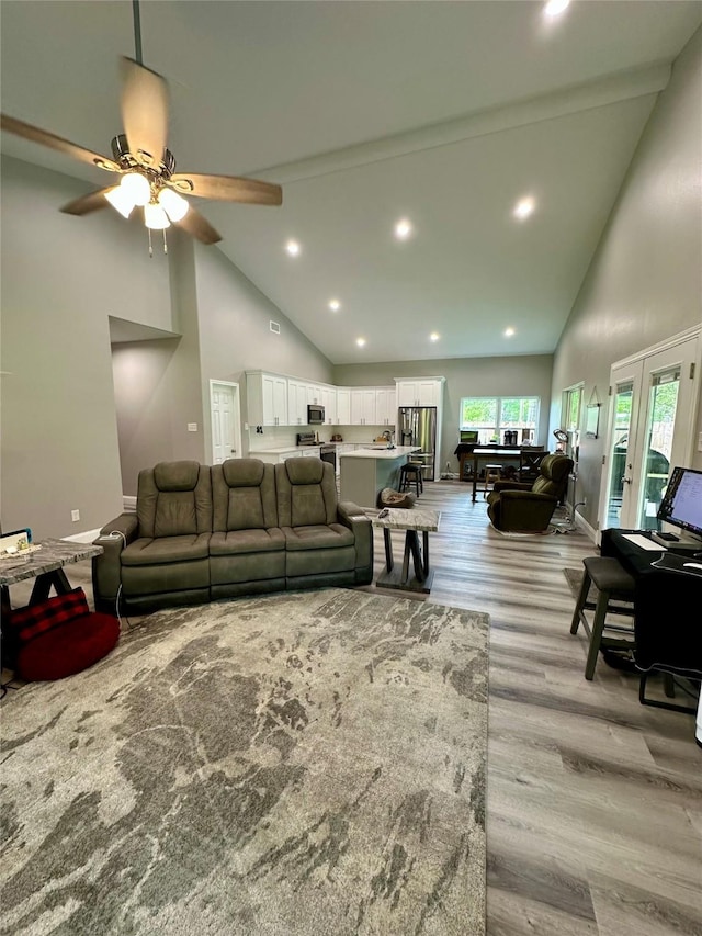 living room featuring light wood finished floors, high vaulted ceiling, baseboards, and a ceiling fan