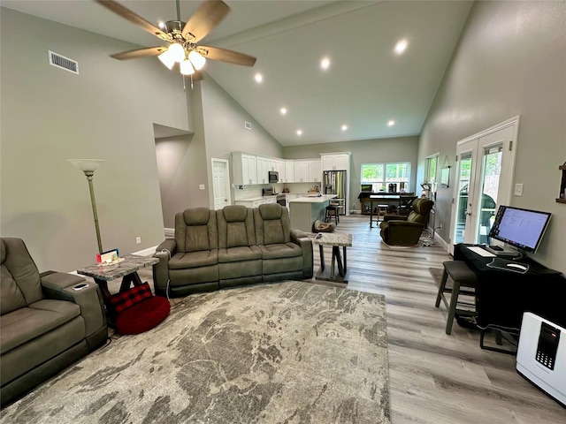 living area with high vaulted ceiling, light wood-type flooring, a ceiling fan, visible vents, and baseboards