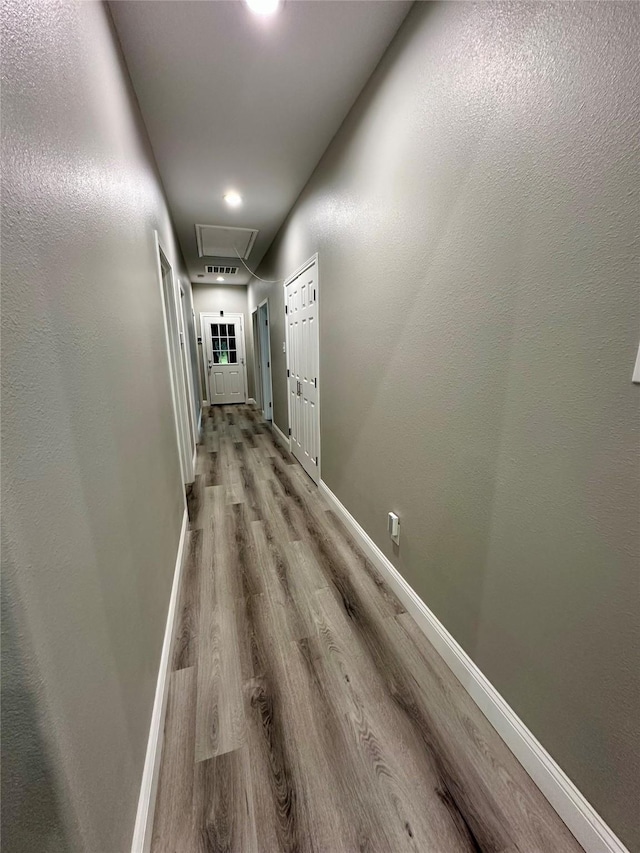 hall with baseboards, attic access, and wood finished floors