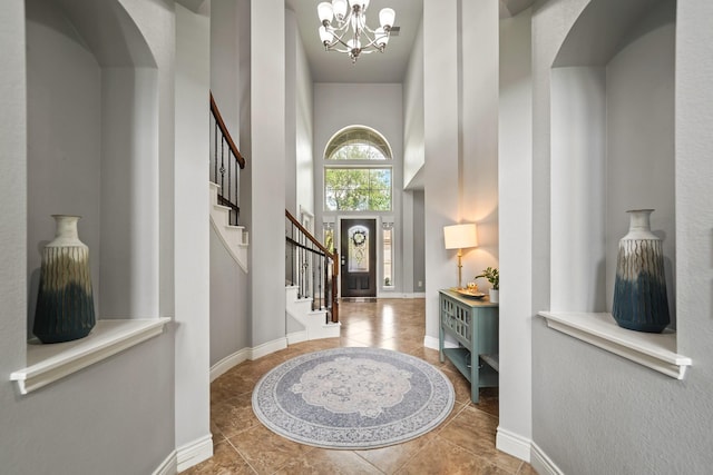 foyer entrance featuring an inviting chandelier, stairs, baseboards, a towering ceiling, and tile patterned flooring