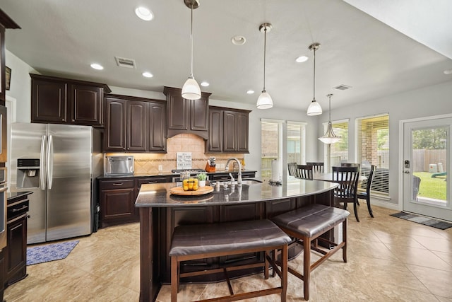 kitchen featuring a breakfast bar, visible vents, stainless steel refrigerator with ice dispenser, backsplash, and dark countertops