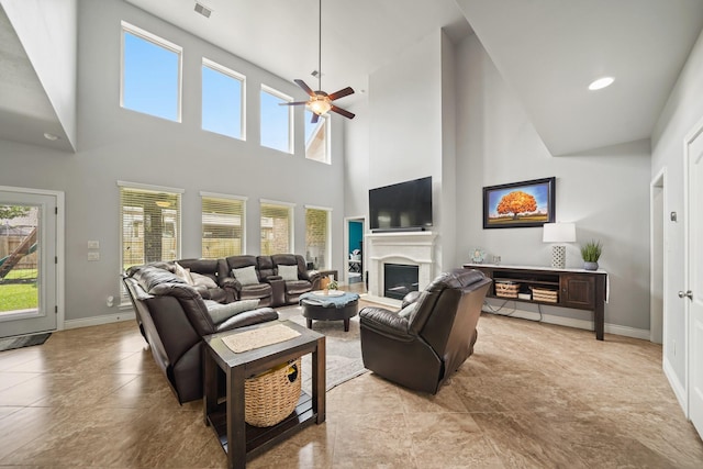 living area featuring baseboards, a wealth of natural light, ceiling fan, and a towering ceiling