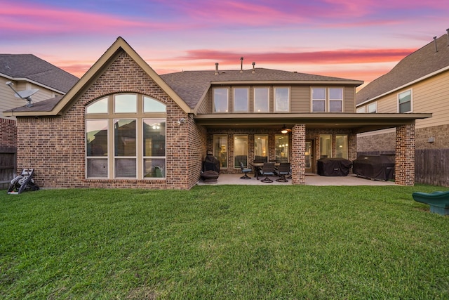back of property at dusk featuring a lawn, fence, a patio area, and brick siding