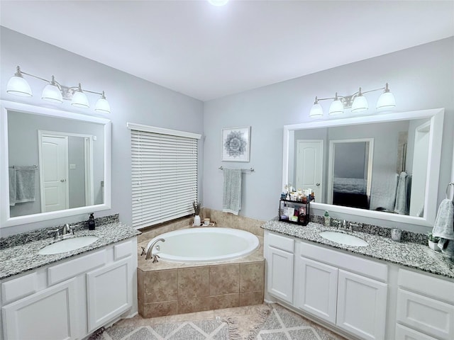 ensuite bathroom featuring two vanities, a garden tub, ensuite bath, and a sink