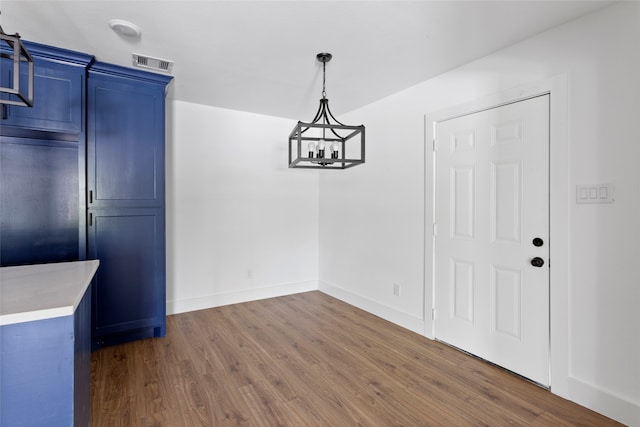 unfurnished dining area with visible vents, baseboards, a notable chandelier, and wood finished floors