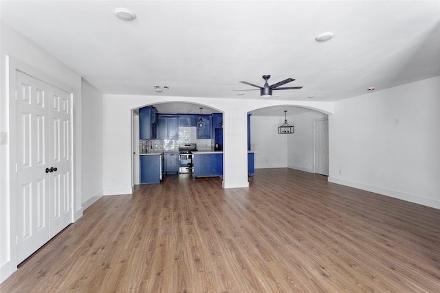 unfurnished living room with arched walkways, baseboards, wood finished floors, and ceiling fan