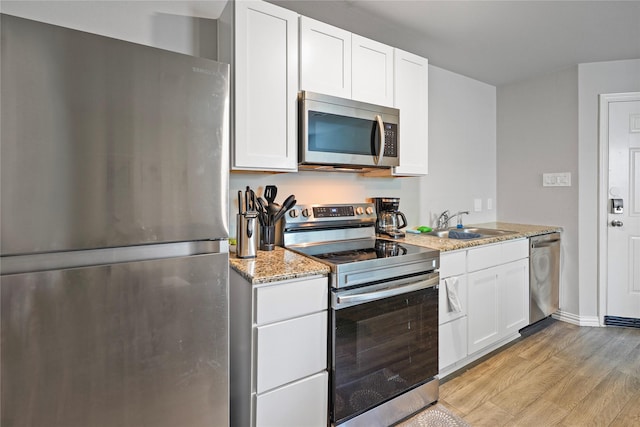 kitchen featuring light stone counters, white cabinets, stainless steel appliances, light wood finished floors, and a sink