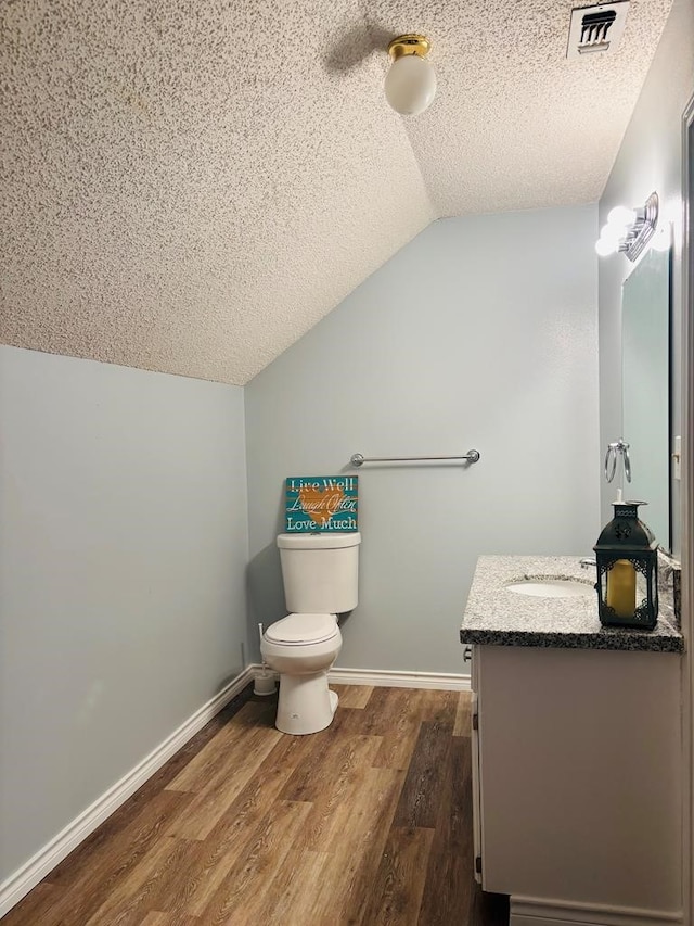 half bath with visible vents, a textured ceiling, vanity, vaulted ceiling, and wood finished floors