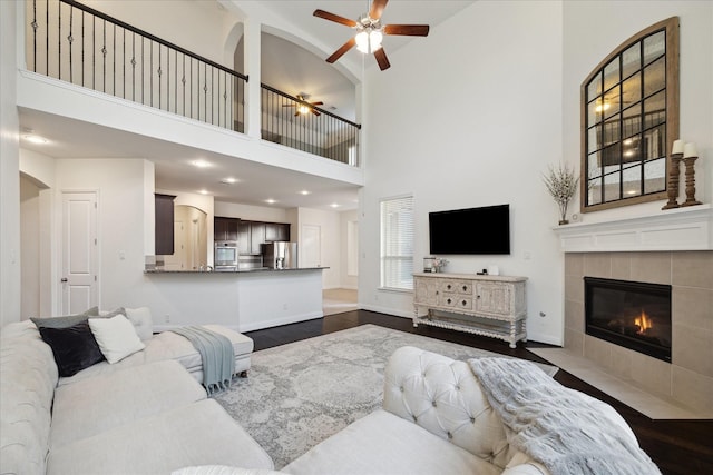living room featuring a ceiling fan, a tile fireplace, baseboards, a high ceiling, and dark wood-type flooring