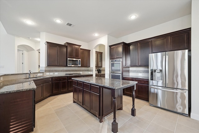 kitchen with a sink, arched walkways, stainless steel appliances, and dark stone counters