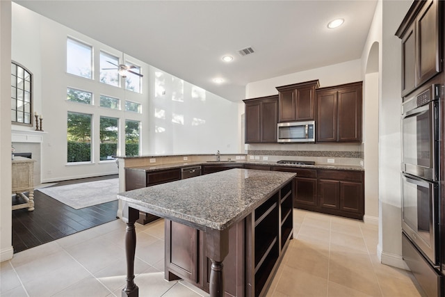 kitchen featuring dark brown cabinets, appliances with stainless steel finishes, light stone counters, a ceiling fan, and a peninsula