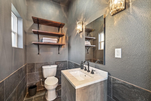 bathroom featuring tile walls, tile patterned flooring, a wainscoted wall, vanity, and toilet