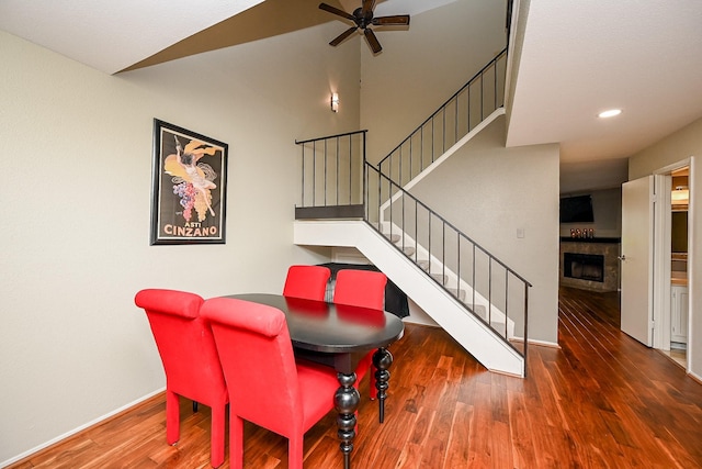 dining area featuring baseboards, stairs, ceiling fan, a tile fireplace, and wood finished floors