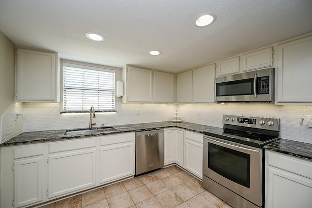 kitchen with stainless steel appliances, a sink, dark stone counters, and decorative backsplash