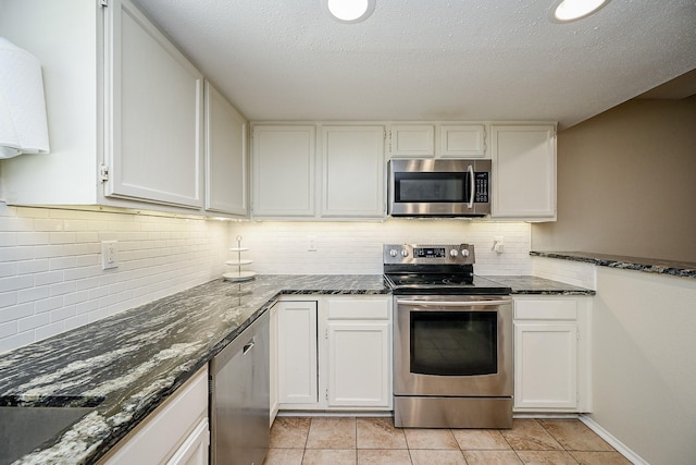 kitchen featuring tasteful backsplash, white cabinetry, dark stone counters, and appliances with stainless steel finishes