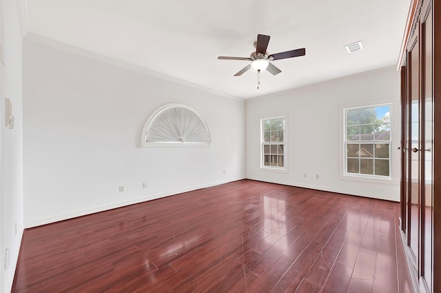 spare room featuring crown molding, ceiling fan, dark wood-type flooring, visible vents, and baseboards