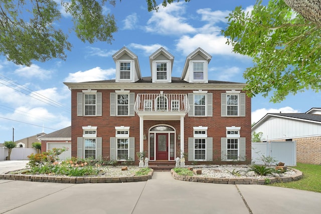 colonial inspired home featuring brick siding, a balcony, and fence
