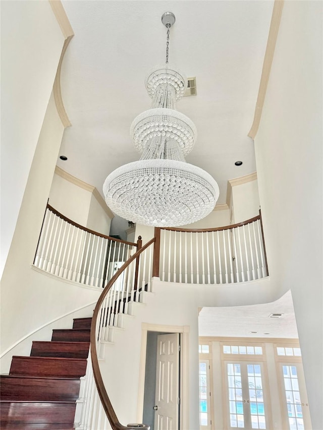 stairway with a high ceiling, crown molding, and an inviting chandelier