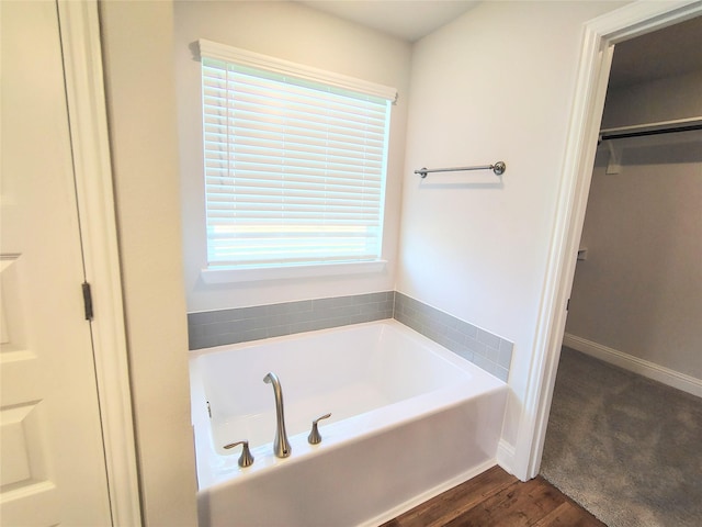 full bathroom featuring baseboards, a garden tub, and wood finished floors